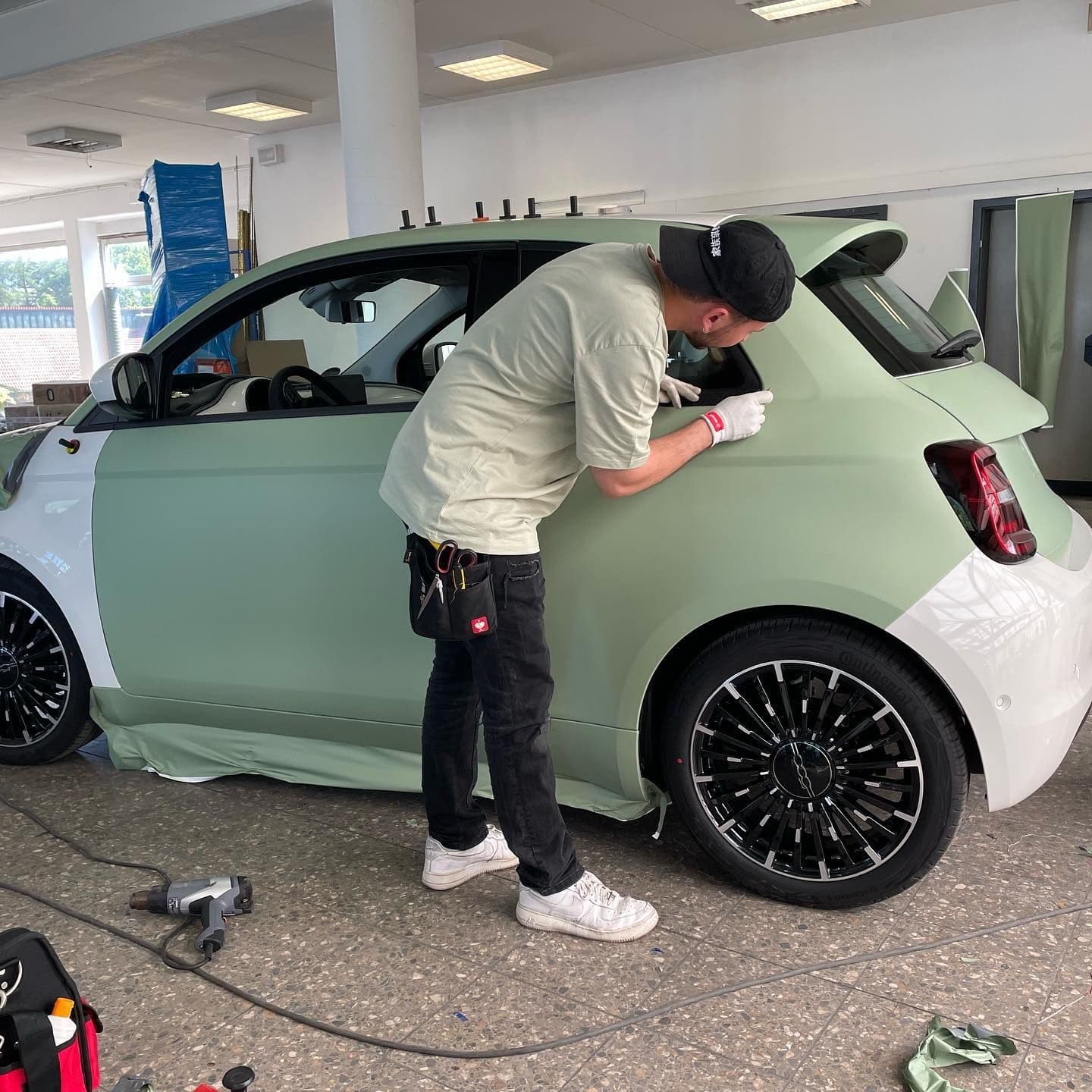 Folierer bringt in der Werkstatt grüne Folie an einem Fiat 500 an