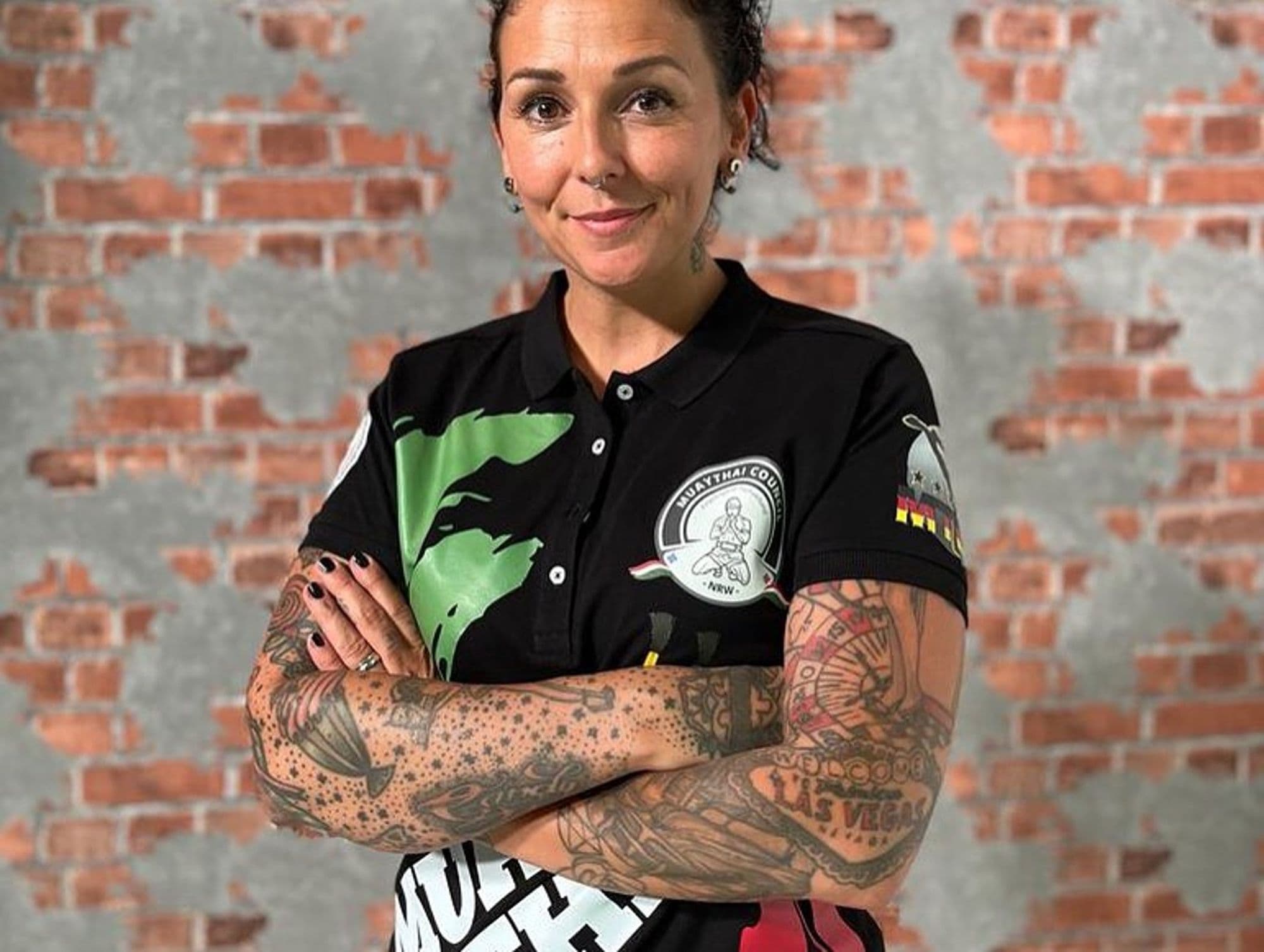 Frau im schwarzen Vereinspoloshirt des Muay Thai Landesverbands NRW vor einer Ziegelwand