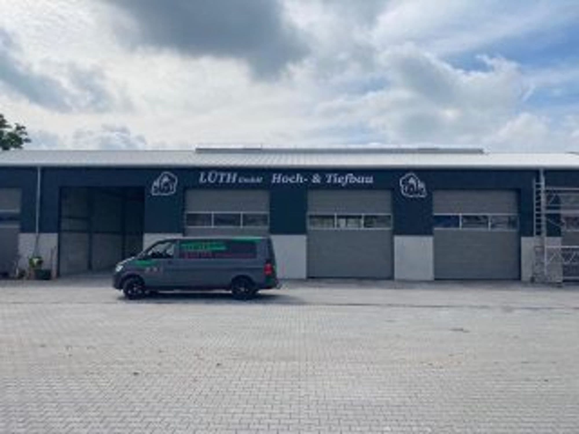 Gewerbehalle mit Firmenschild an der Fassade, davor ein beschrifteter Lieferwagen