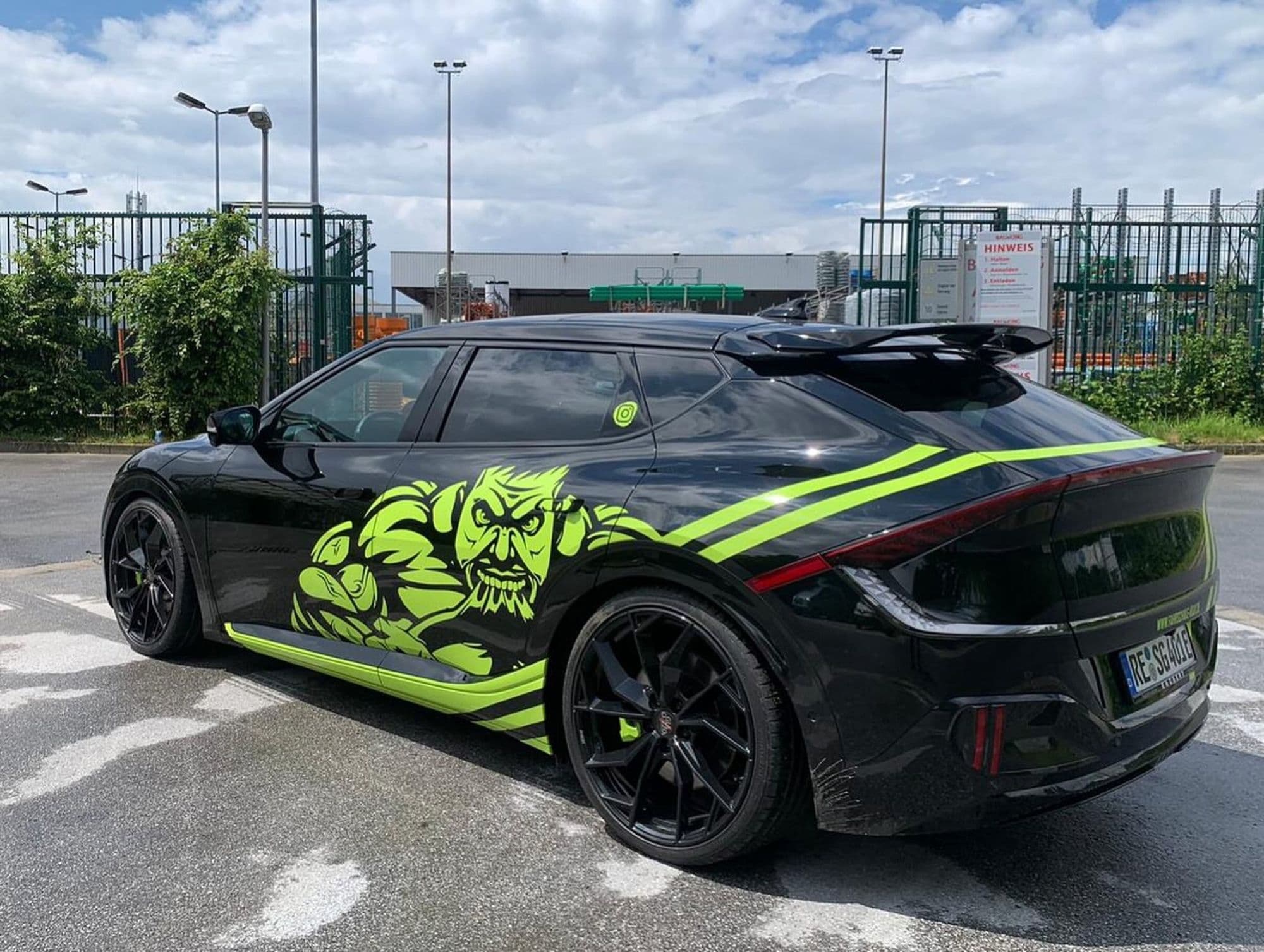 Schwarzer Kia EV6 mit neongelbem Monster-Design und Streifen, geparkt auf nassem Asphalt.
