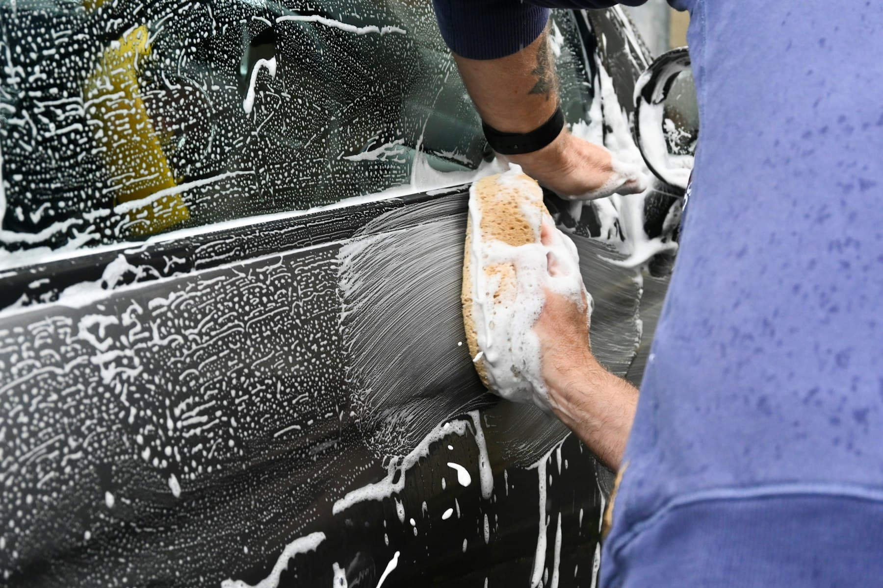Autotür wird mit Schwamm und Seifenschaum von Hand gereinigt