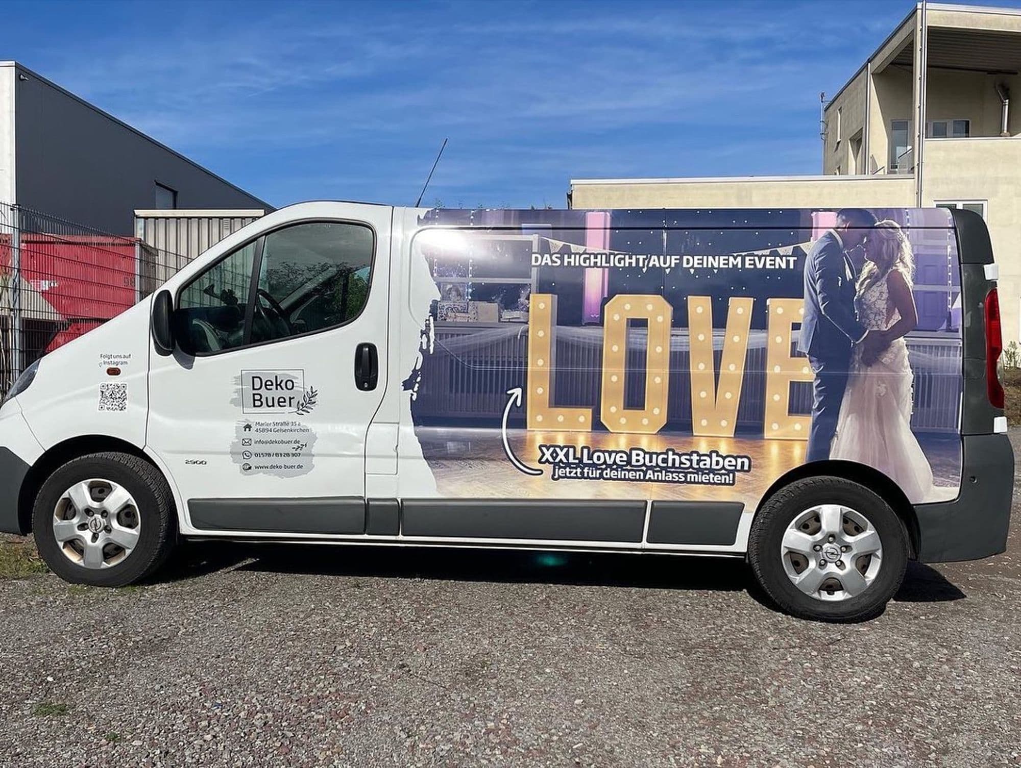 Weißer Lieferwagen mit der Aufschrift „Deko Bauer“ und einer großen LOVE-Leuchtschrift auf der Seite.