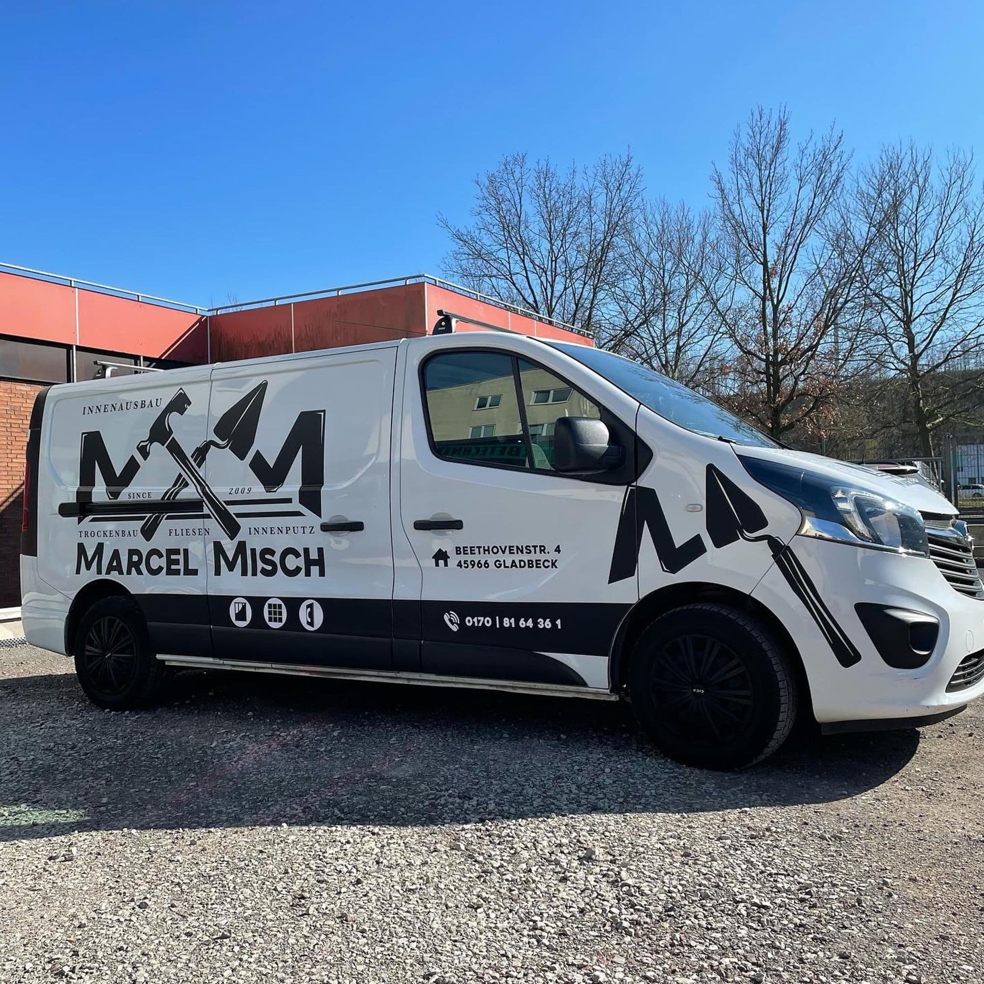 Weißer Lieferwagen mit schwarzem Firmenlogo „Misch Marcel Misch“, Bauwerkzeugsymbolen und Kontaktinformationen.